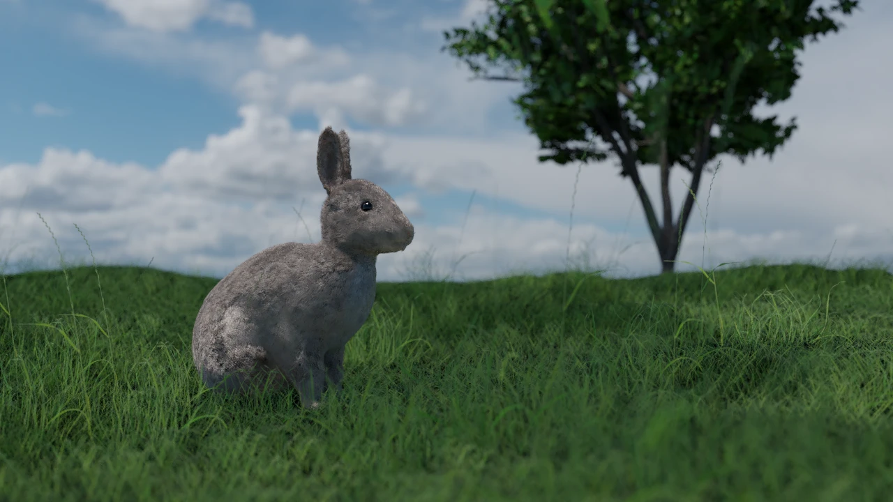 A dark grey bunny sitting in a grass. In the background there is a single tree, which is quite blurry. Above all of it there are white clouds on a bright blue sky.